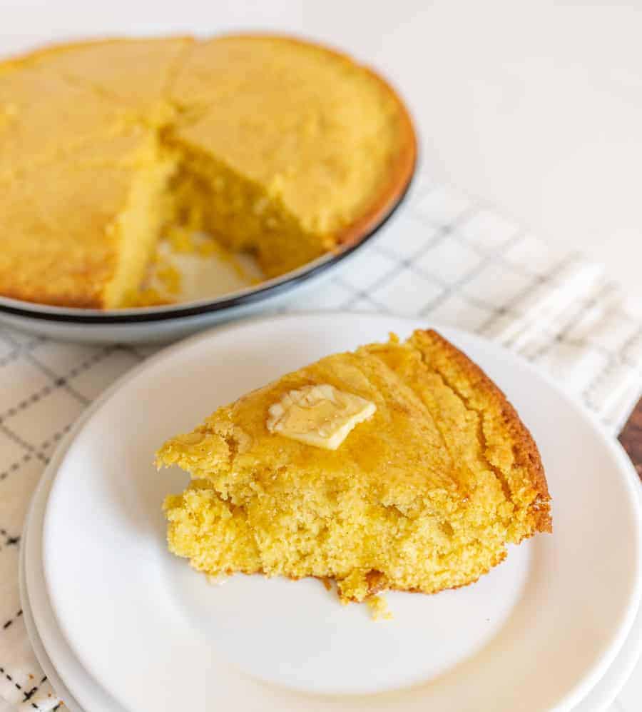 sliced sourdough cornbread on white plate with butter and honey on top