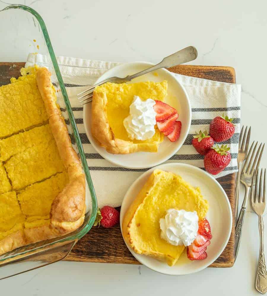 german pancakes cut and served on white plate with strawberries and whipped cream on top