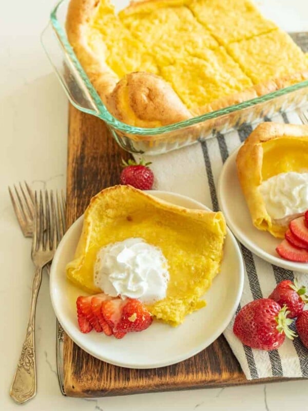german pancakes cut and served on white plate with strawberries and whipped cream on top