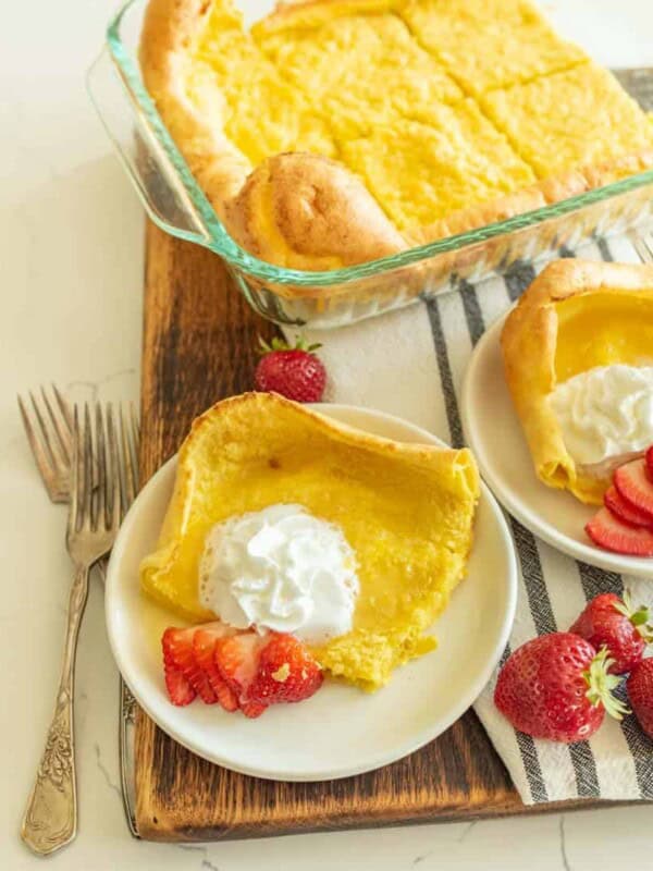 german pancakes cut and served on white plate with strawberries and whipped cream on top