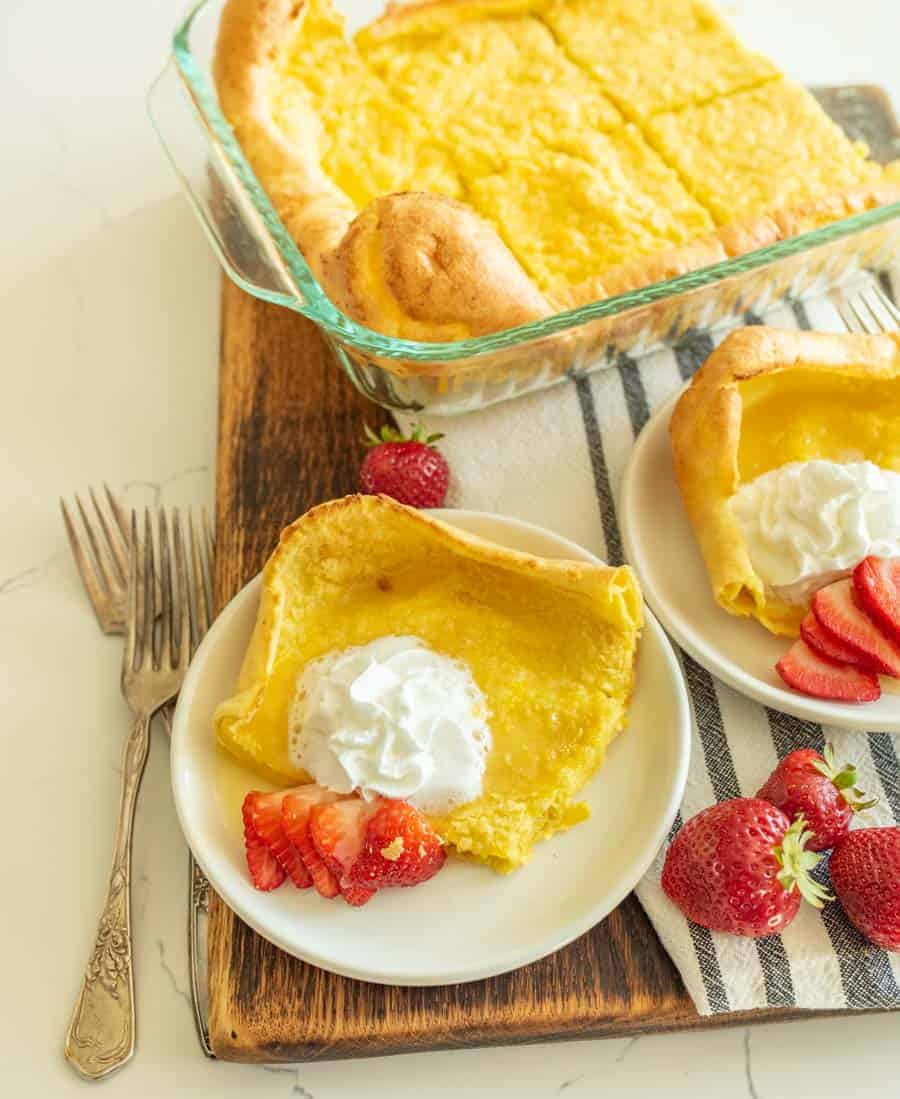 german pancakes cut and served on white plate with strawberries and whipped cream on top