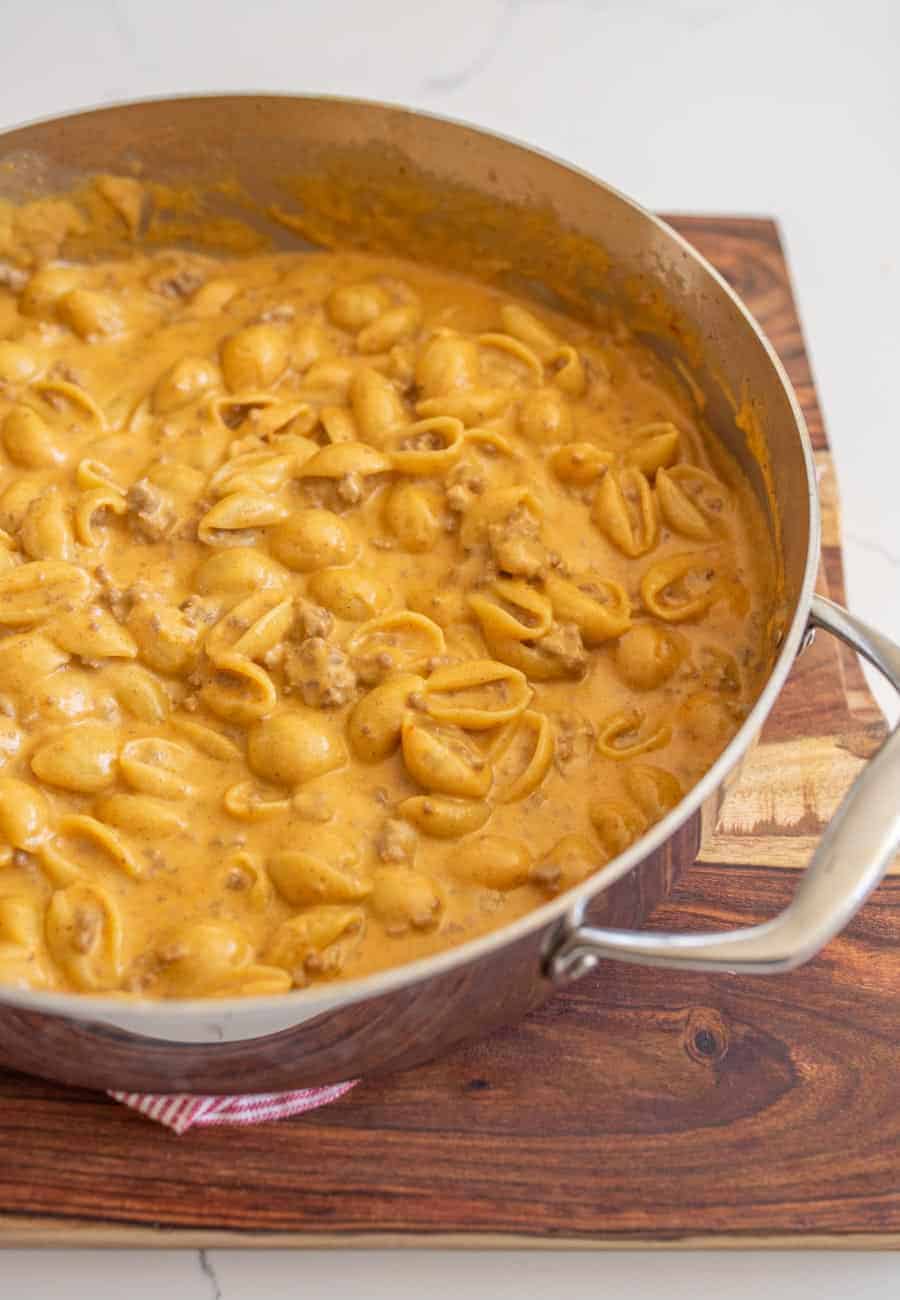 A close-up of finished hamburger helper dish in a large skillet on a wooden cutting board.