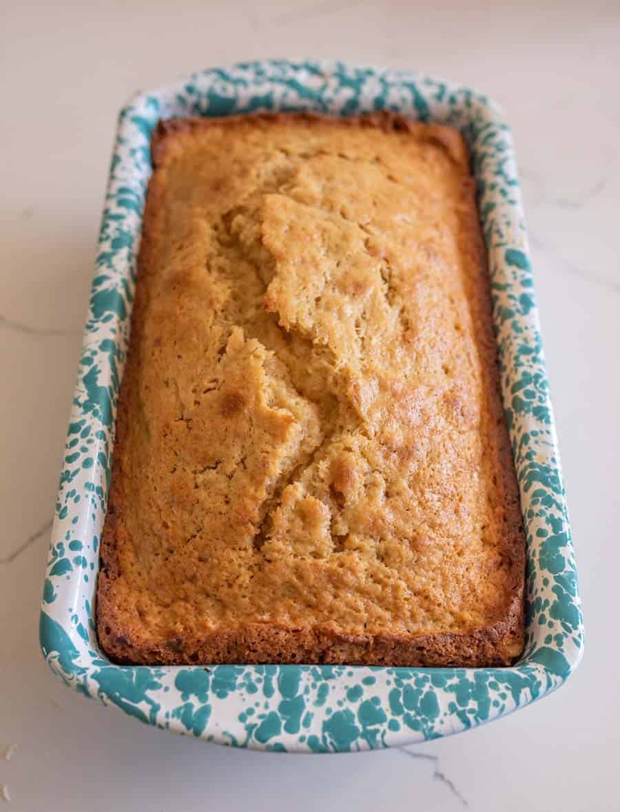 A whole baked sourdough banana bread in a speckled white and blue bread pan.