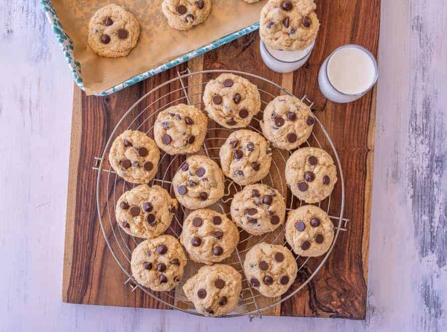 baked sourdough chocolate chip cookies on a cooling rack with glassed of milk next to them