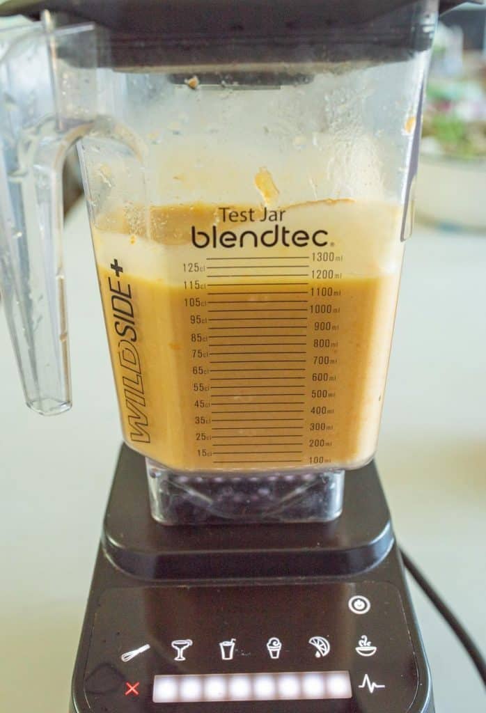 A Blendtec blender jar filled with a thick orange mixture sits on its base, perfect for making  homemade fruit leather snacks for kids. The jar features measurement markings and the label Test Jar, while the control panel lights show it&rsquo;s powered on.