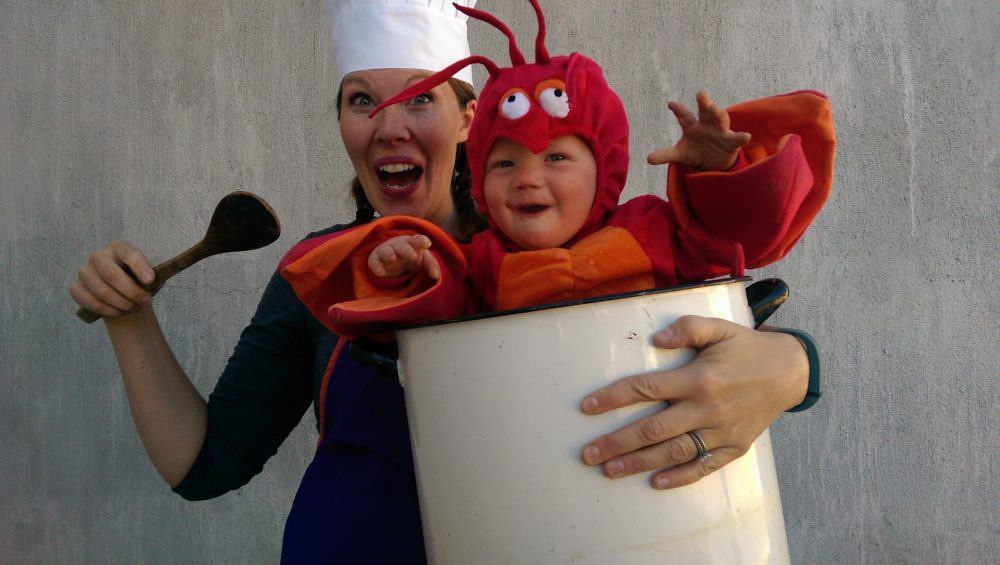 woman with a chefs hat with a baby dressed as a lobster in a pot Halloween costume. 