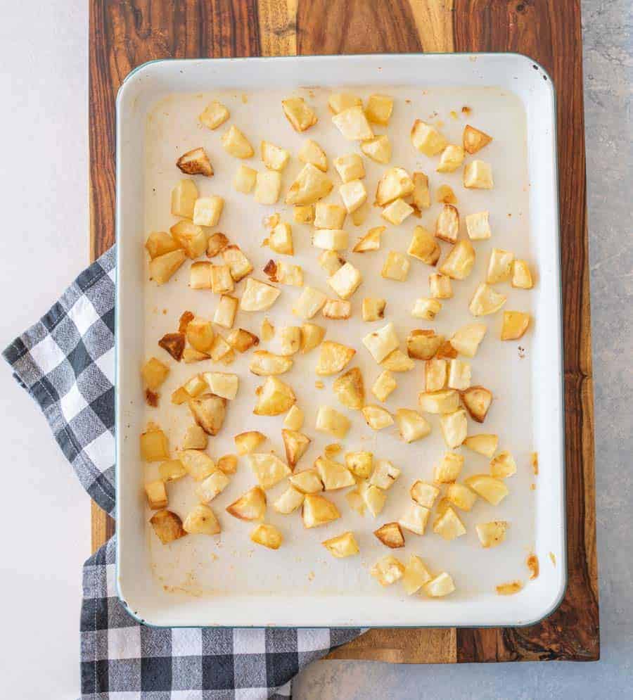 crispy oven roasted potato cubes on enamel baking sheet on gingham tablecloth on wood cutting board