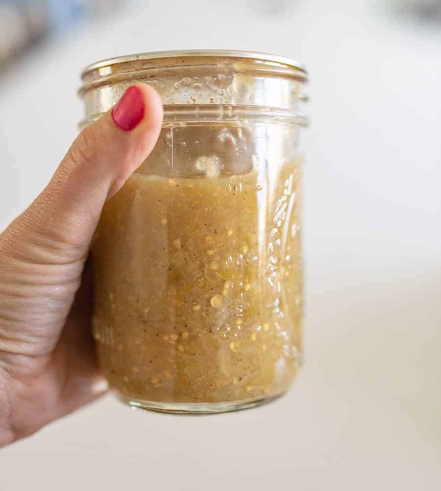 A hand holding jar of tomatillo salsa.