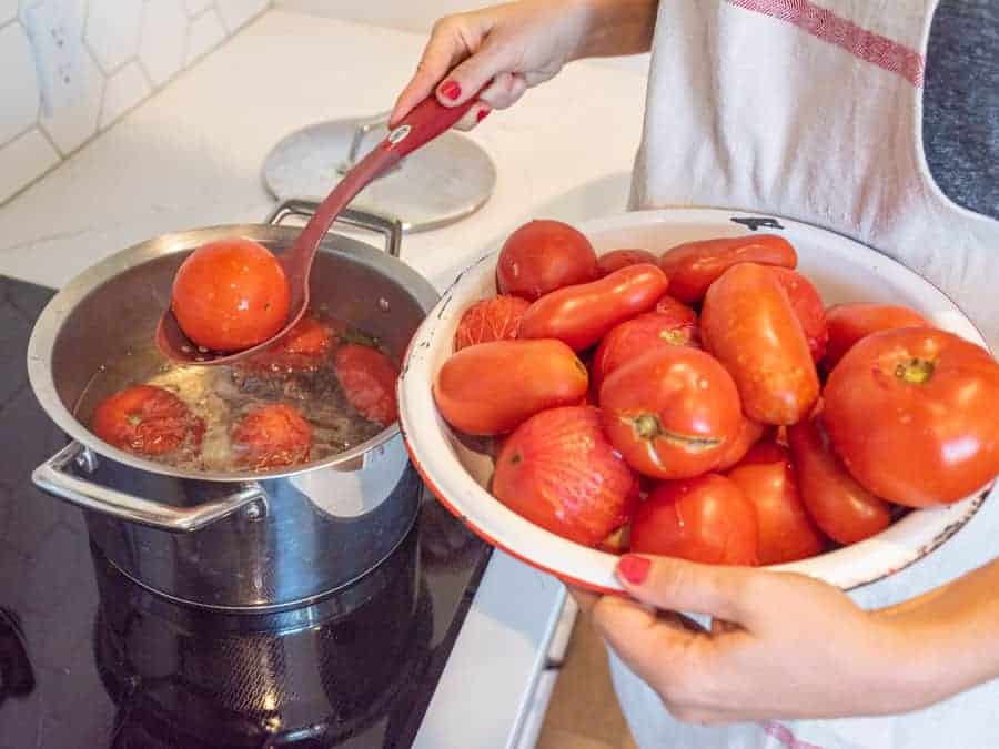 spoon removing blanched tomato from water bath