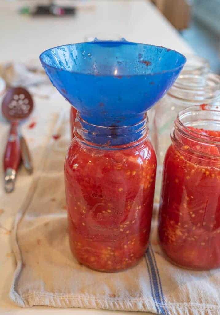 blue funnel in glass jar being filled with tomatoes