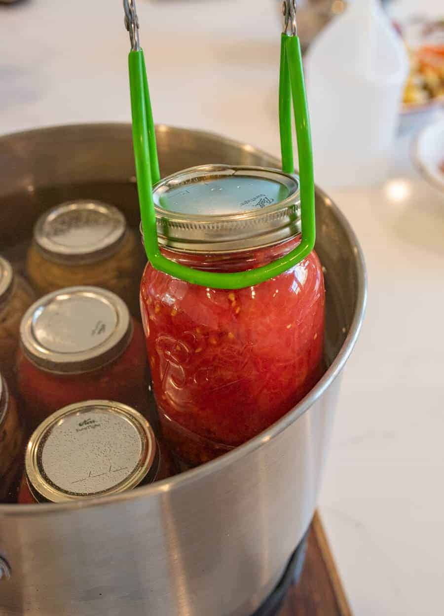 tongs being used to pull hot finished jar from water bath canner