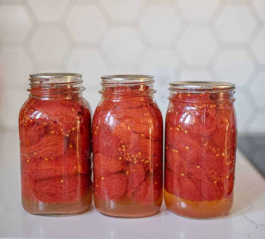 three finished jars of tomatoes sitting in a row