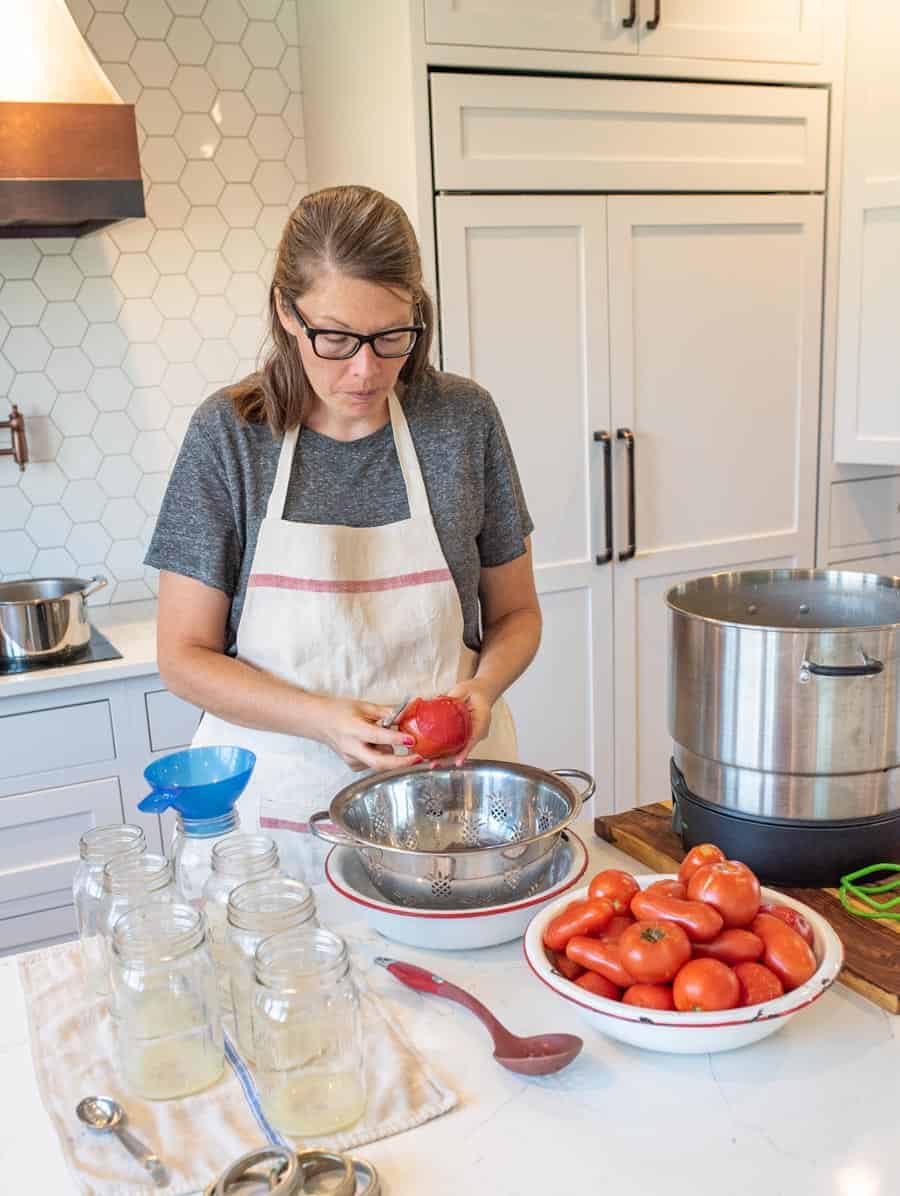 woman peeling tomato for canning with supplies near her