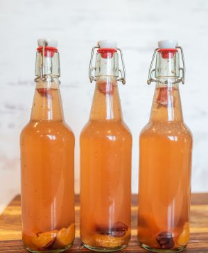 thee wire lid carafe bottles of orange second ferment kombucha with oranges and cherries in the bottom