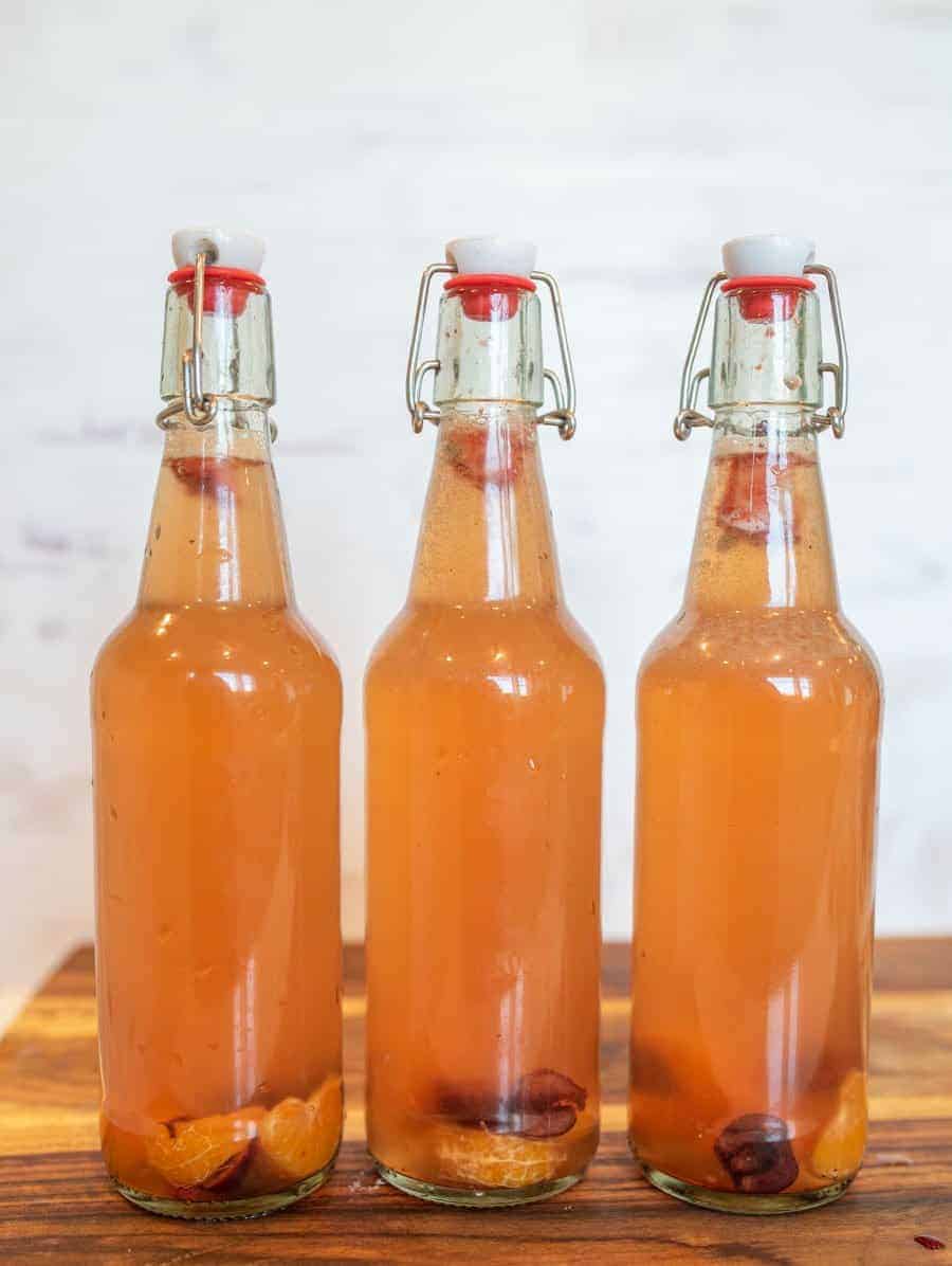 thee wire lid carafe bottles of orange second ferment kombucha with oranges and cherries in the bottom for how to make kombucha.