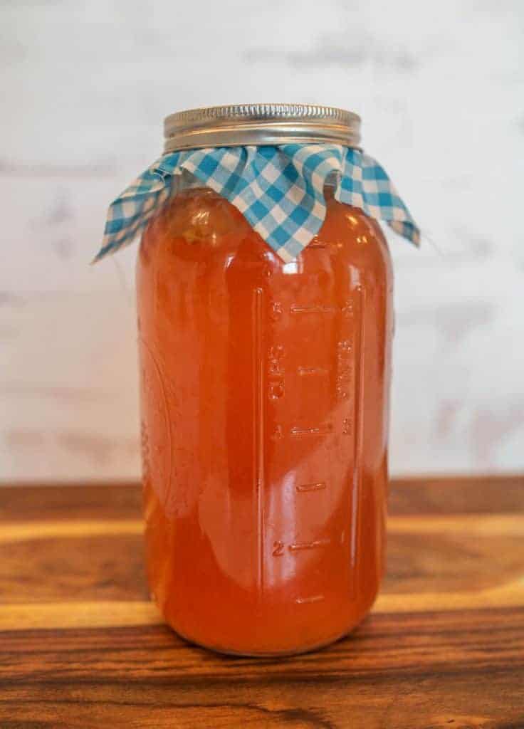 half gallon mason jar filled with first ferment kombucha and capped with gingham cloth and metal ring