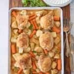 oven roasted chicken thighs, carrots, potatoes, and onions on enamel baking sheet with dinner plates, forks, and garnish