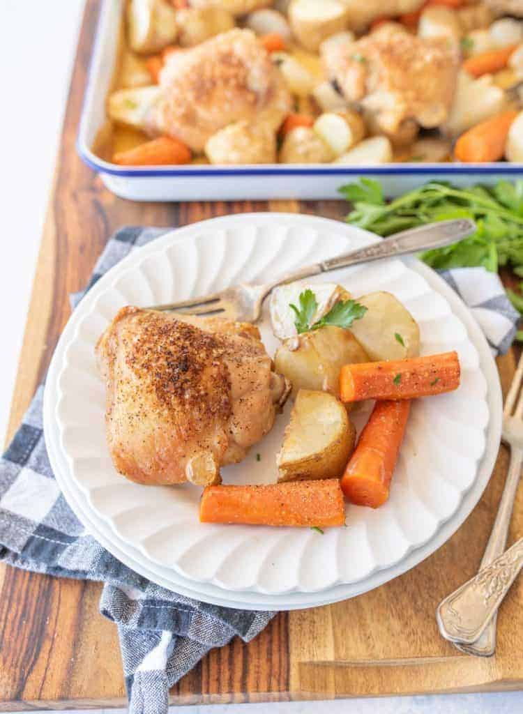 oven roasted chicken thighs, carrots, potatoes, and onions on enamel baking sheet and dinner plate with fork and garnish