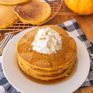 pile pf pumpkin pancakes on white plate with whipped cream