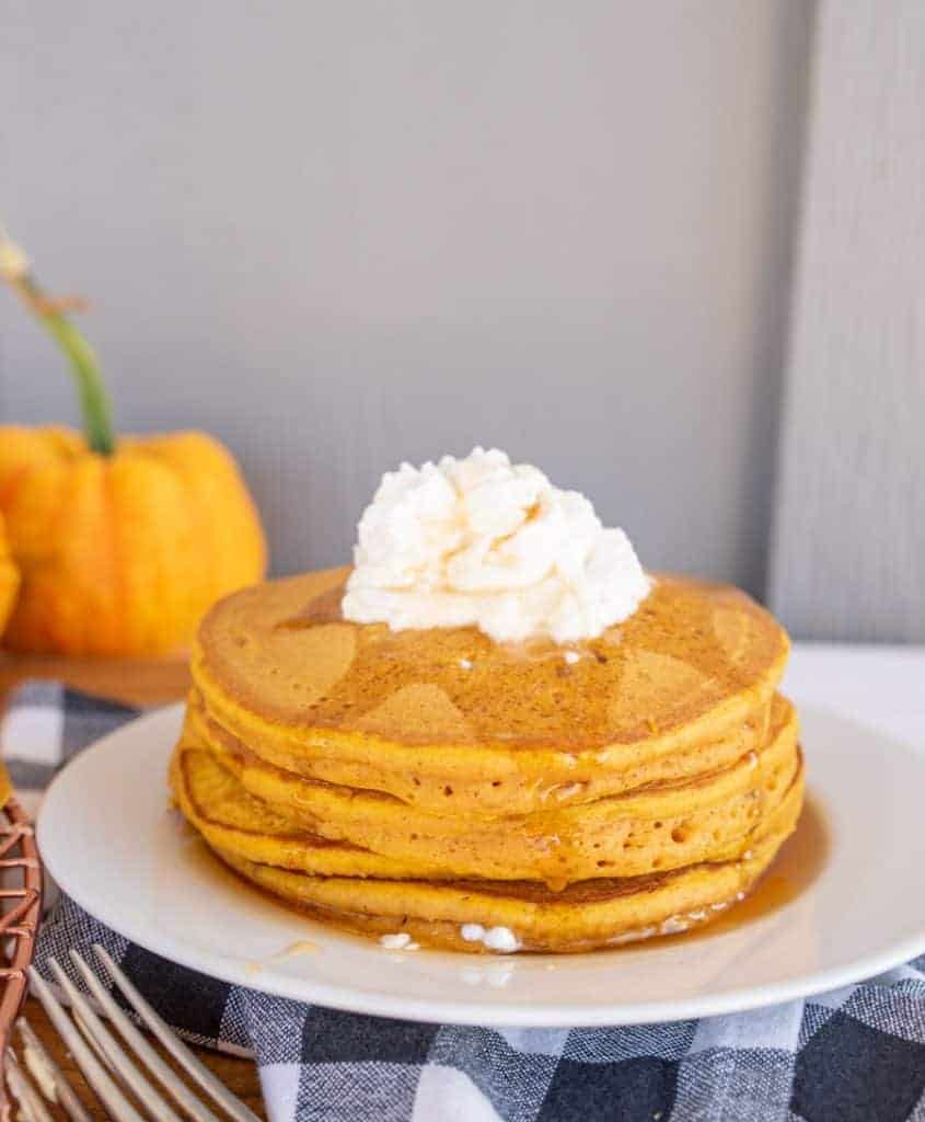 pile pf pumpkin pancakes on white plate with whipped cream