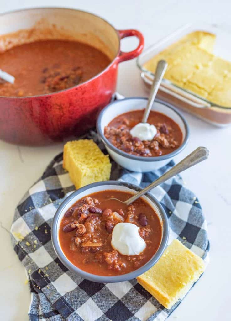 two bowls of chili with cornbread and the iron pot with chili in it
