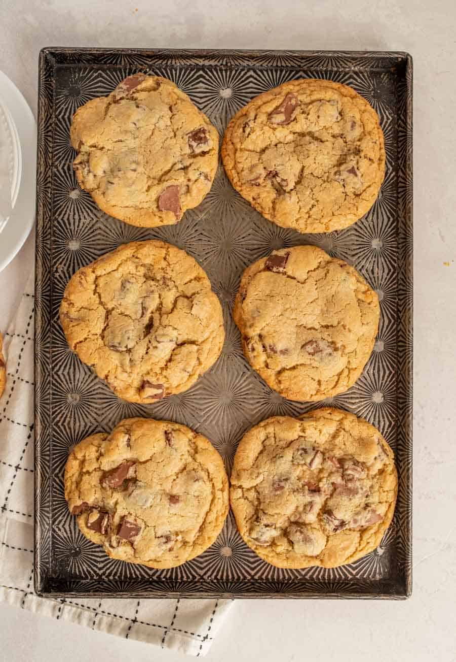 Six baked giant chocolate chunk cookies on a baking sheet.
