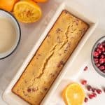 loaf of cranberry orange bread in white loaf pan surrounded by oranges and cranberries