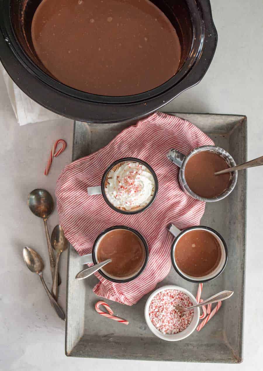 top view of tray of mugs filled with crock pot hot chocolate next to the crock pot of hot chocolate