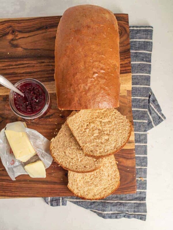 a whole wheat bread loaf with three slices cut with butter and jam next to it.