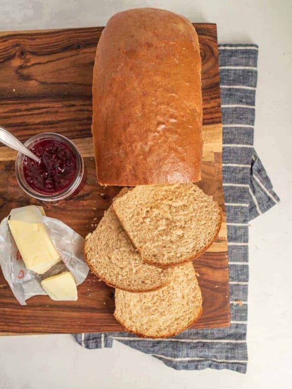 top view of whole wheat bread loaf with three slices cut with butter and jam next to it