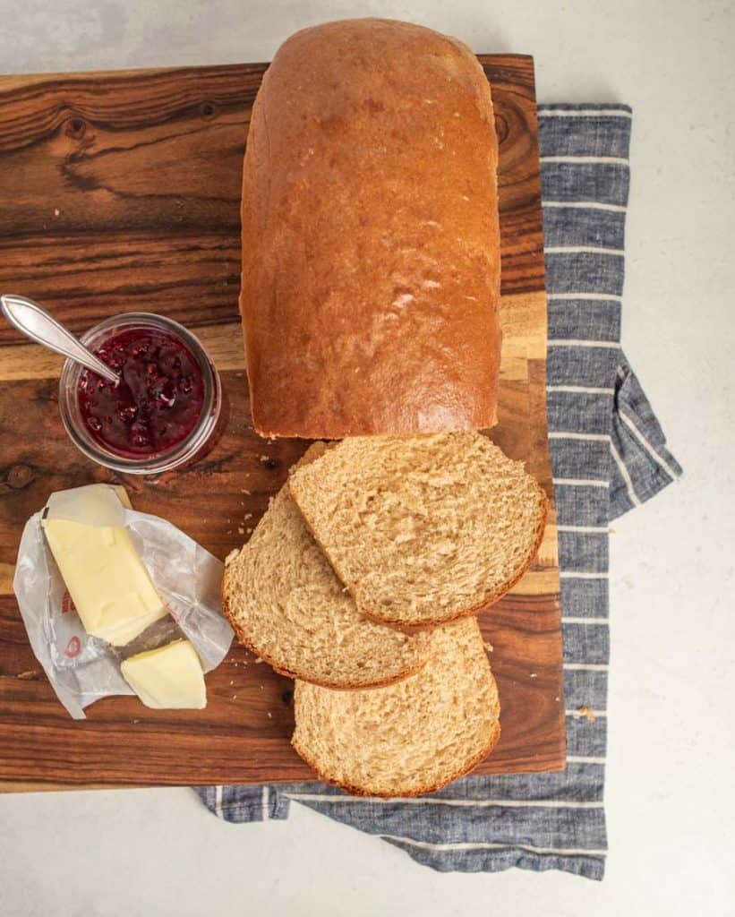 top view of whole wheat bread loaf with three slices cut with butter and jam next to it