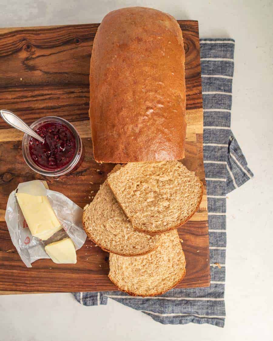 top view of whole wheat bread loaf with three slices cut with butter and jam next to it