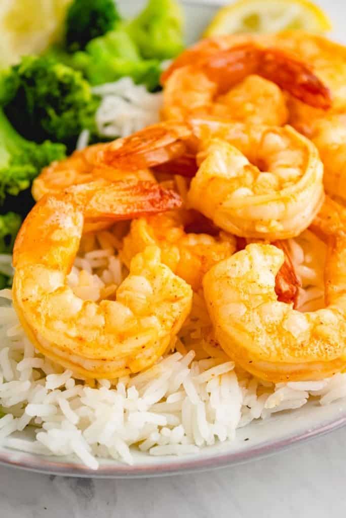 close up of dish with cooked garlic shrimp over white rice and broccoli to the side