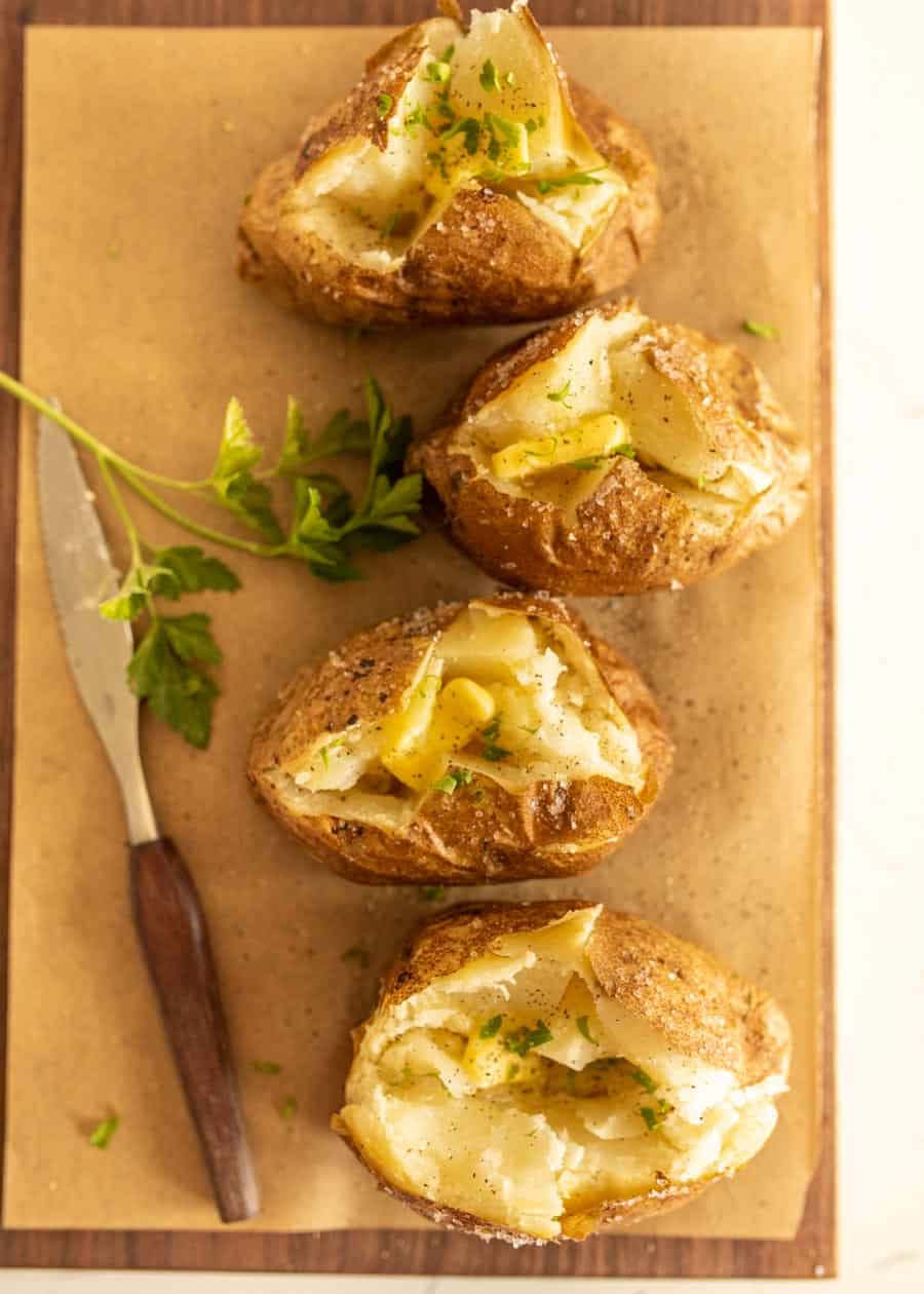 top view of baked potatoes with butter on board with knife