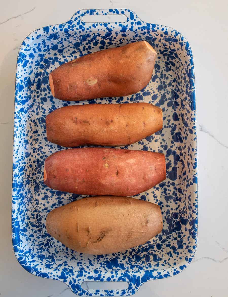 Four raw sweet potatoes in a blue and white speckled baking dish.