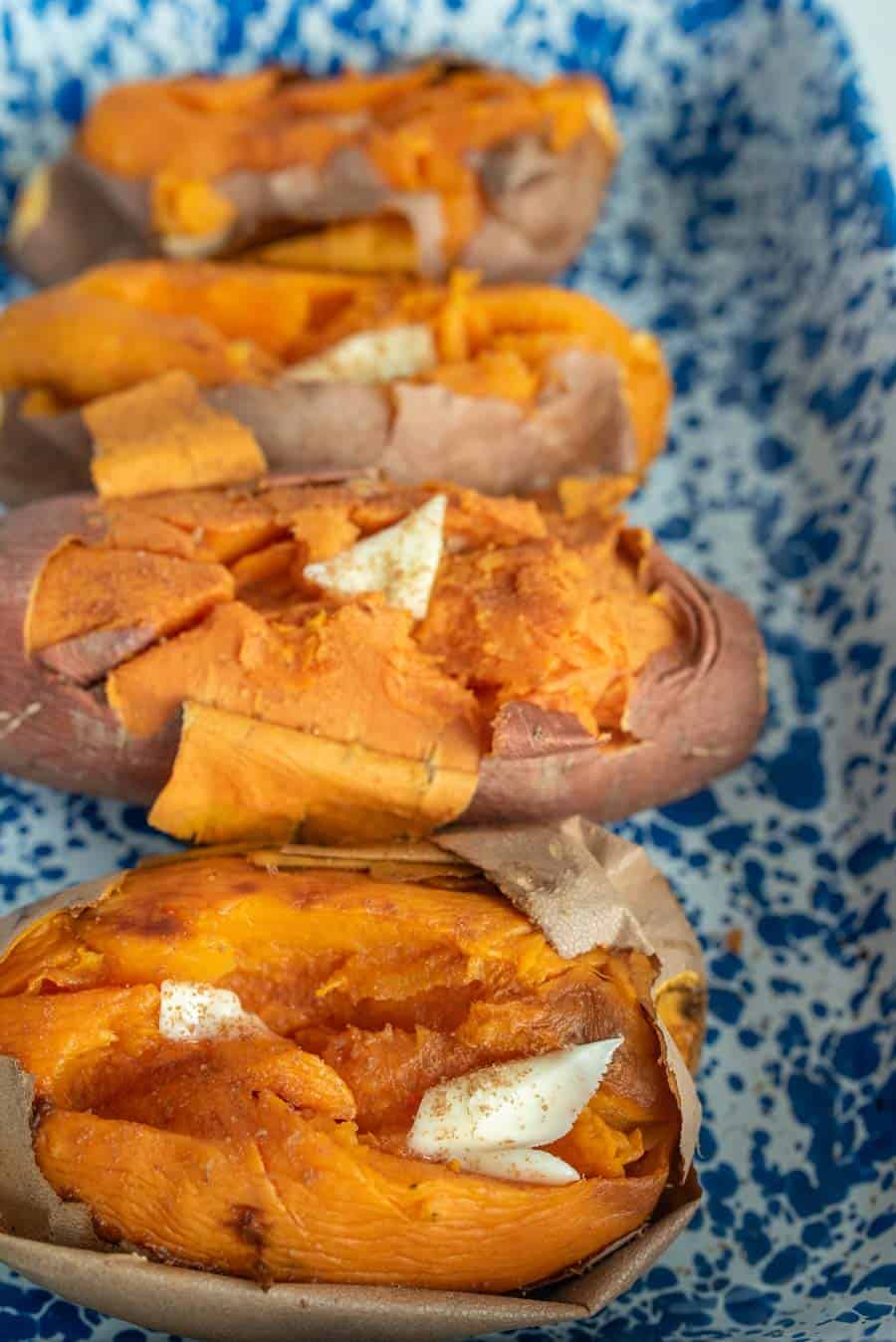Four baked sweet potatoes with butter on them in a white baking dish with blue speckles.