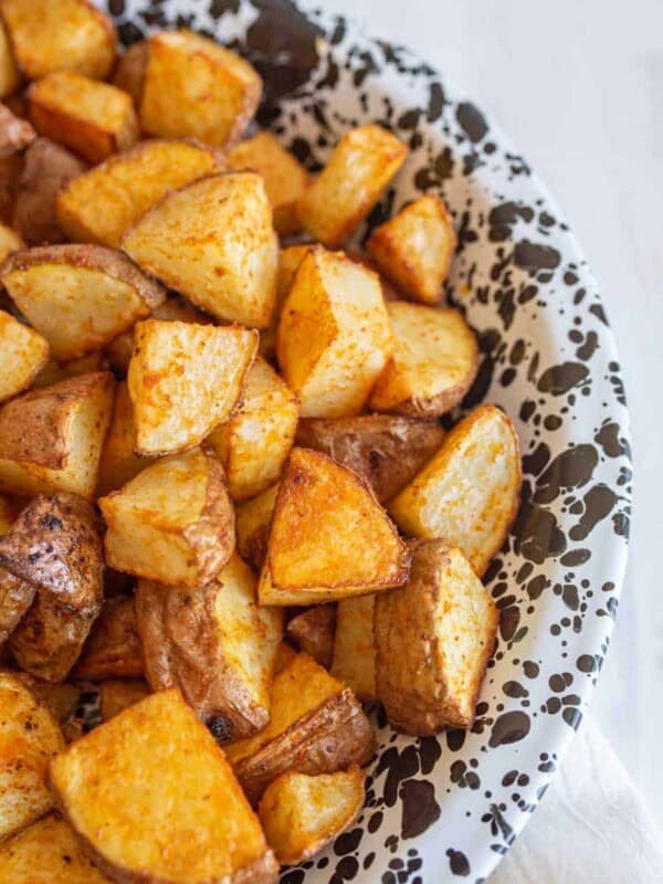 A close-up of a plate filled with oven roasted red potatoes, golden brown with seasoning, served on a white dish with black speckles.