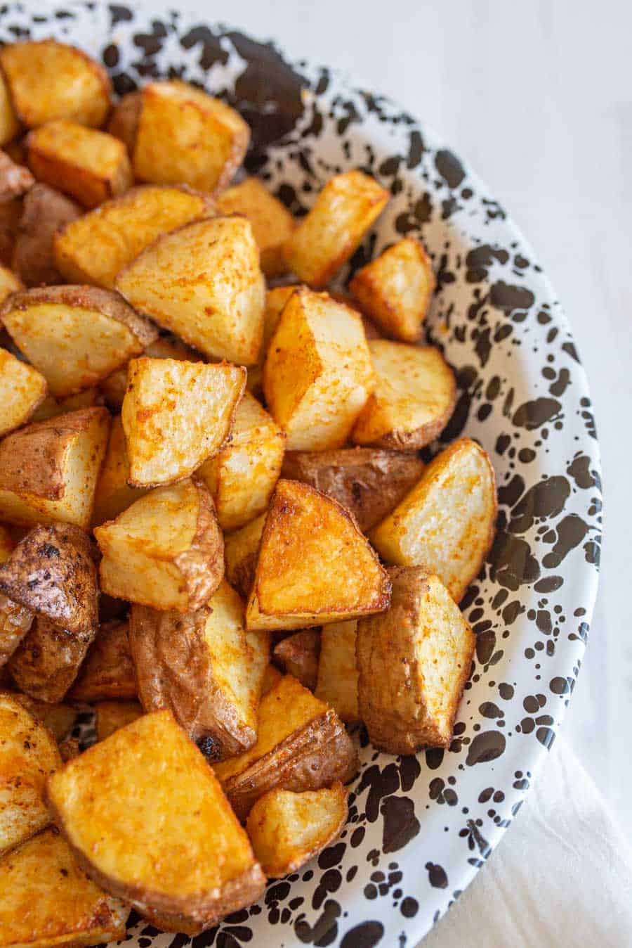 Roasted red potatoes in a white bowl with black speckles.