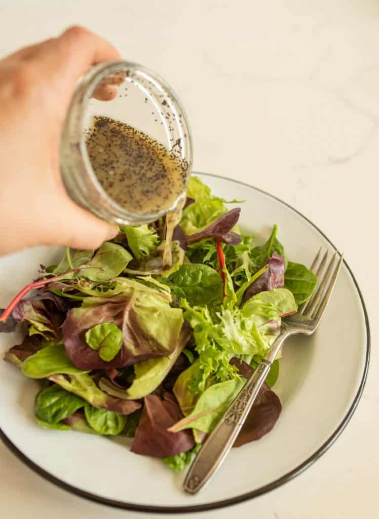 hand pouring salad dressing over a plate of salad