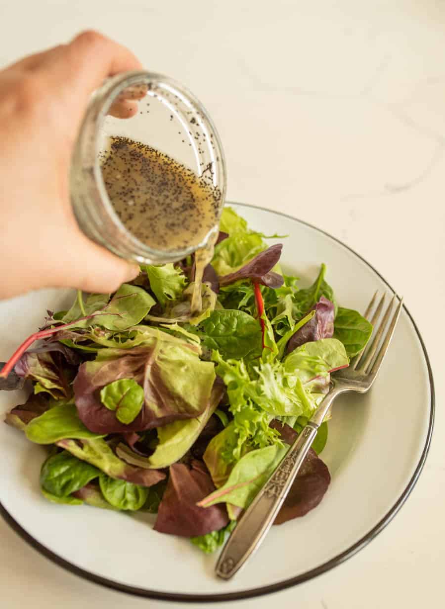 hand pouring salad dressing over a plate of salad.