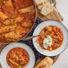 top down view of lasagna soup in pan next to two bowls and a loaf of french bread