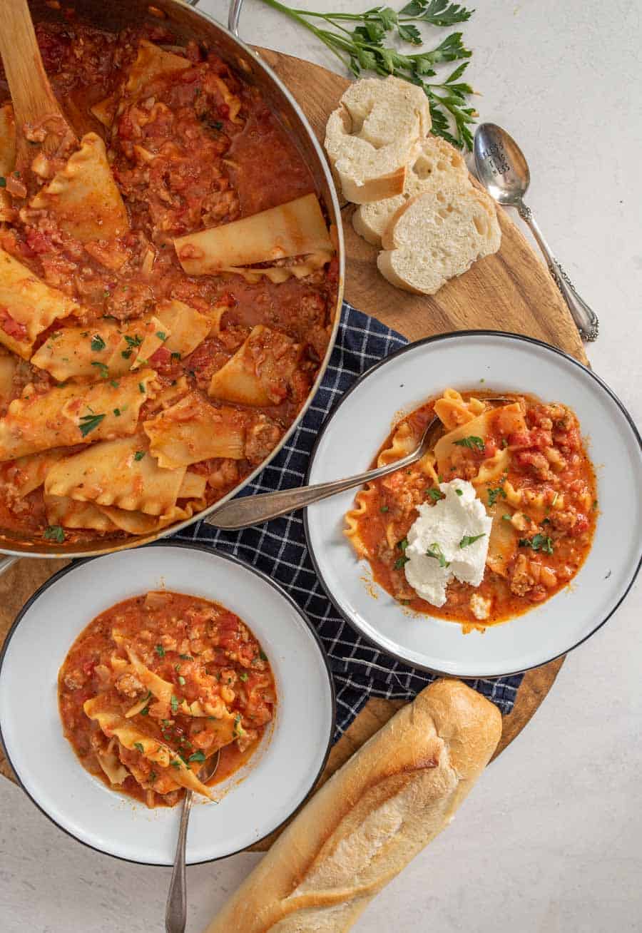 top down view of lasagna soup in pan next to two bowls and a loaf of french bread