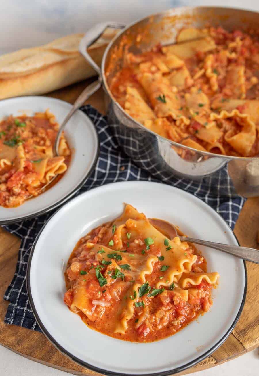 lasagna soup in white bowls with parsley on top next to a pot of lasagna soup