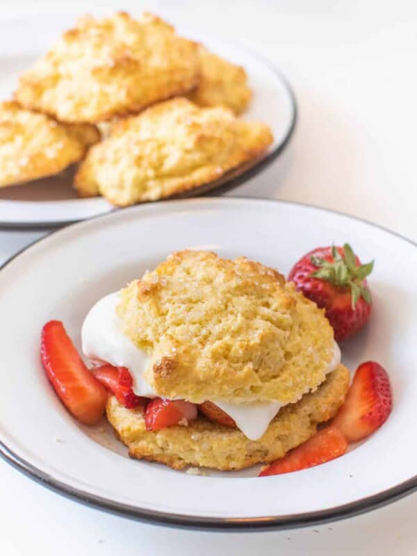 A bowl with a strawberry short cake biscuit, whipped cream, and sliced strawberries featuring a biscuit recipe for strawberry shortcake.