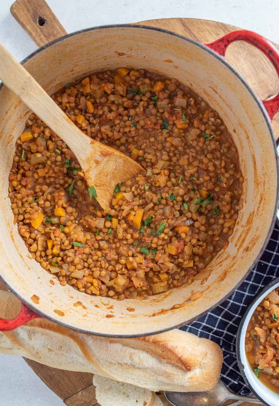 Vegetarian lentil soup in large pot with wood spoon in it.