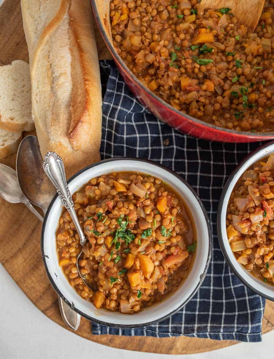 top view of a white bowl filled with vegetarian lentil soup with pot of lentil soup and loaf of French bread