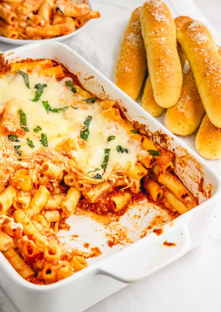 baking dish with baked ziti in it with breadsticks in the background