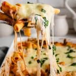 Baked ziti being scooped out of baking dish with a cheese pull