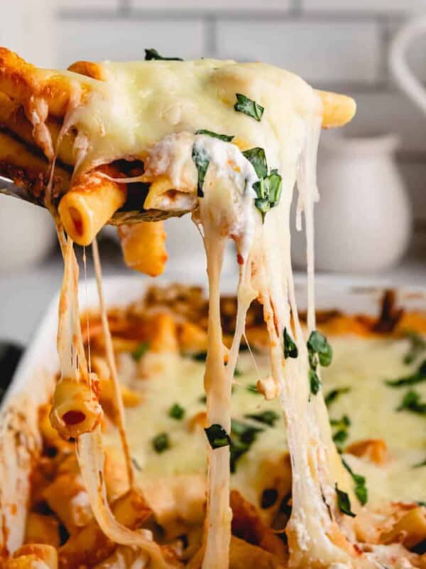 Baked ziti being scooped out of baking dish with a cheese pull