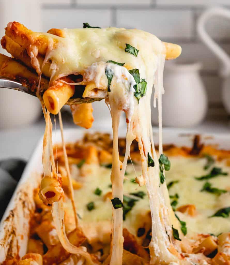 Baked ziti being scooped out of baking dish with a cheese pull